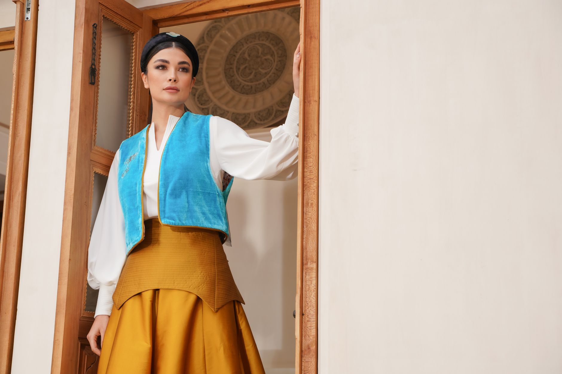 A woman in traditional Iranian attire stands gracefully indoors, showcasing a blend of modern and classic fashion styles.