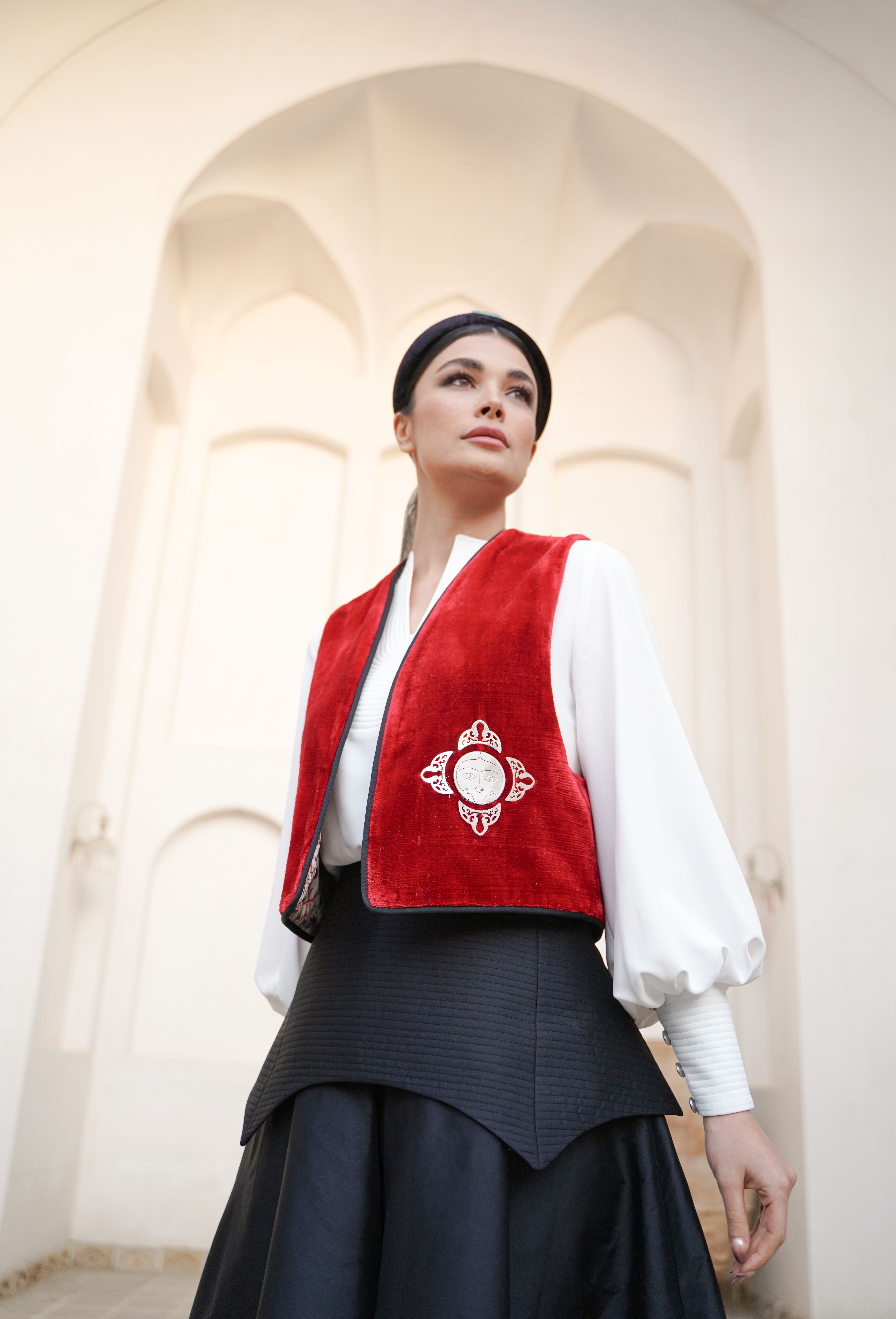 Woman in traditional Persian attire stands against Kashan architecture, showcasing elegant fashion.