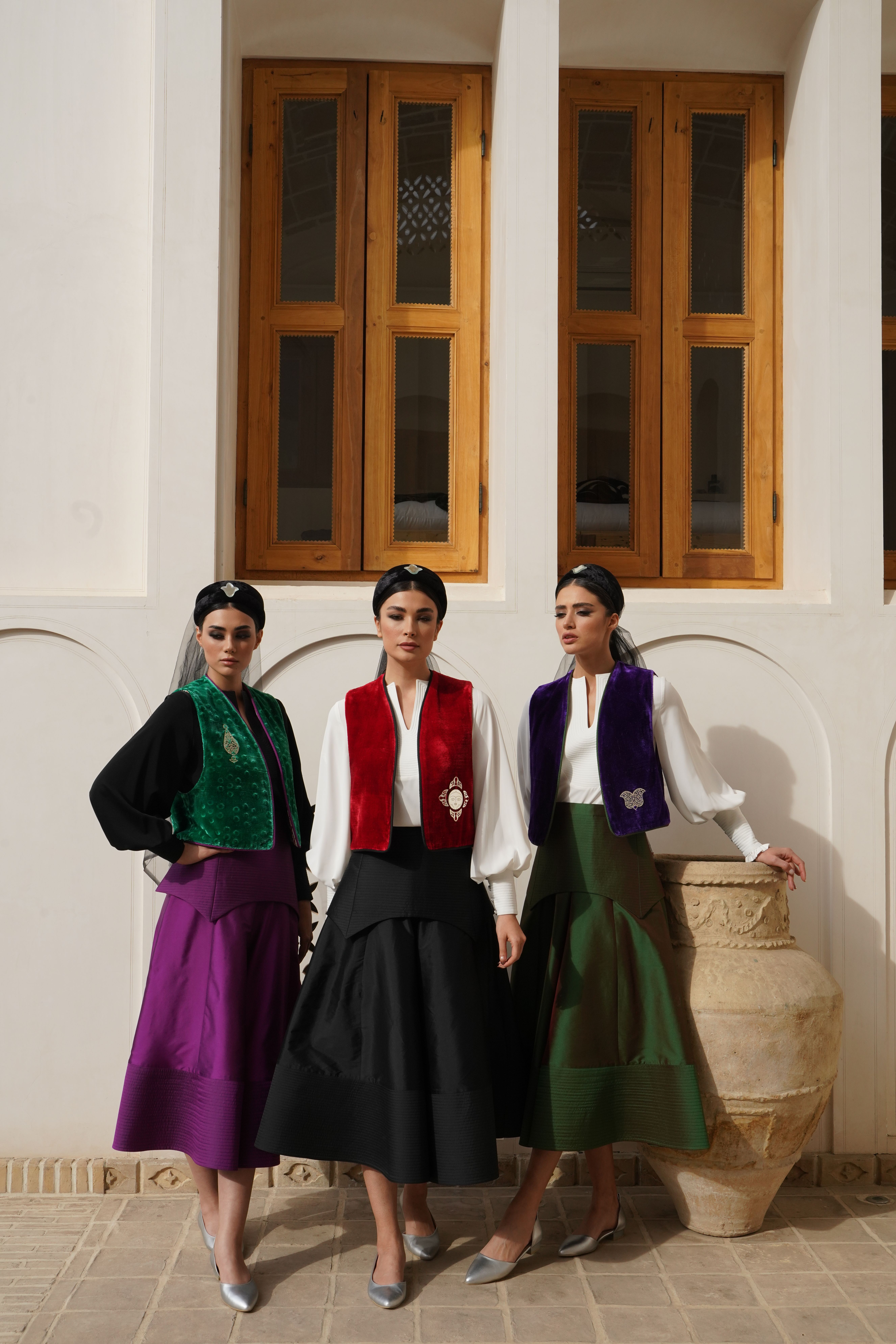 Three women pose in colorful traditional dresses with a classic building backdrop.