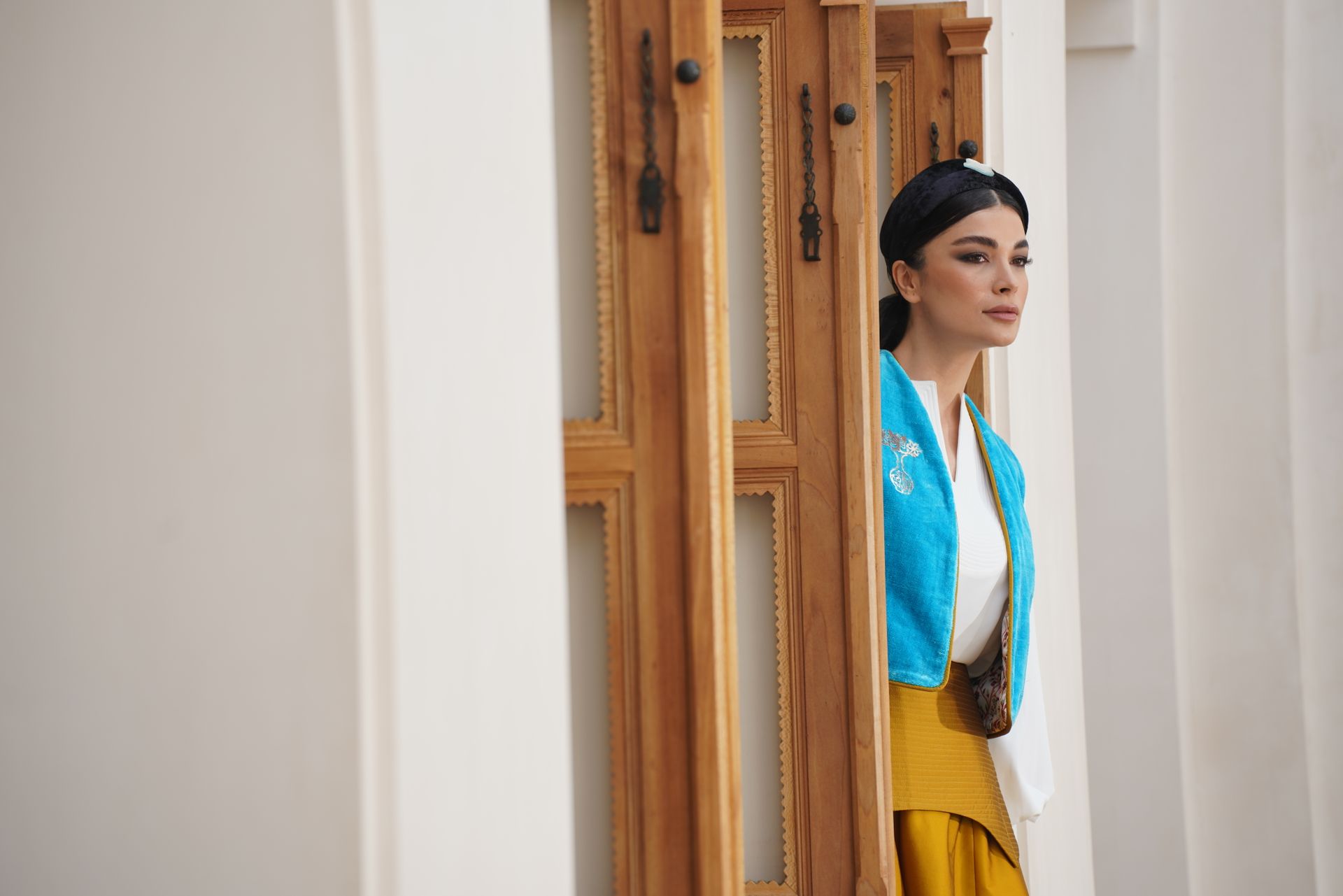 A woman elegantly posing in traditional Persian fashion with blue vest and white blouse.