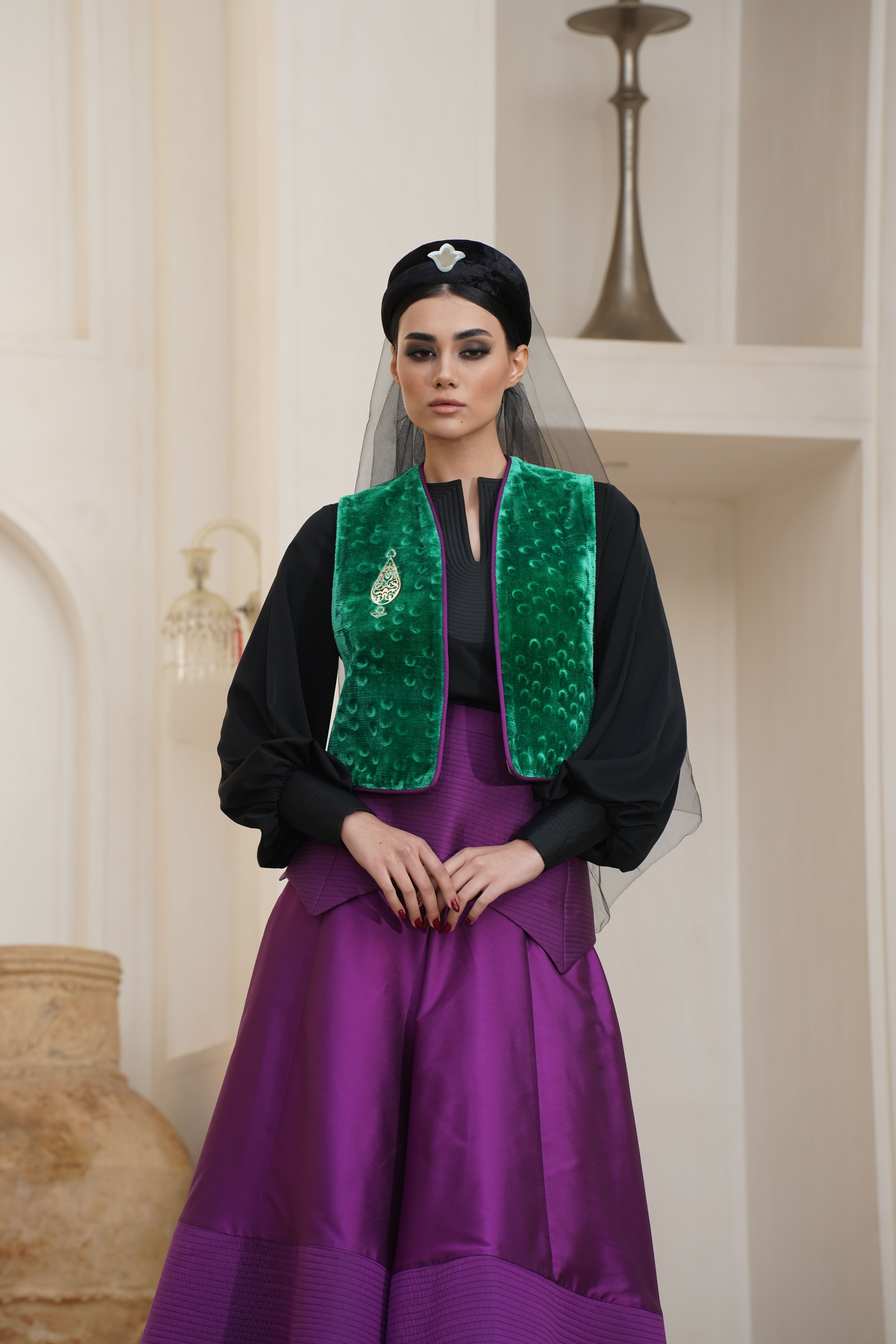 Portrait of a woman in traditional fashion, wearing a green vest and veil indoors.