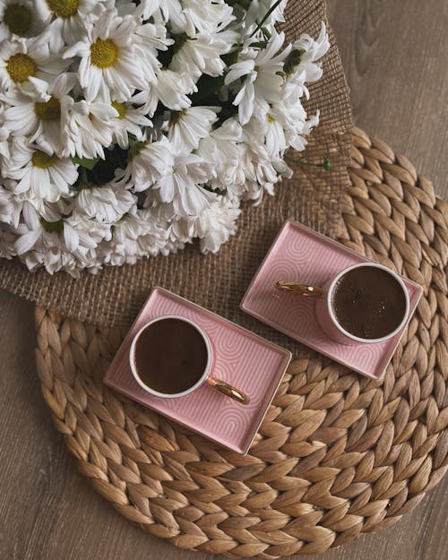 Two pink cups with flowers on a pink table
