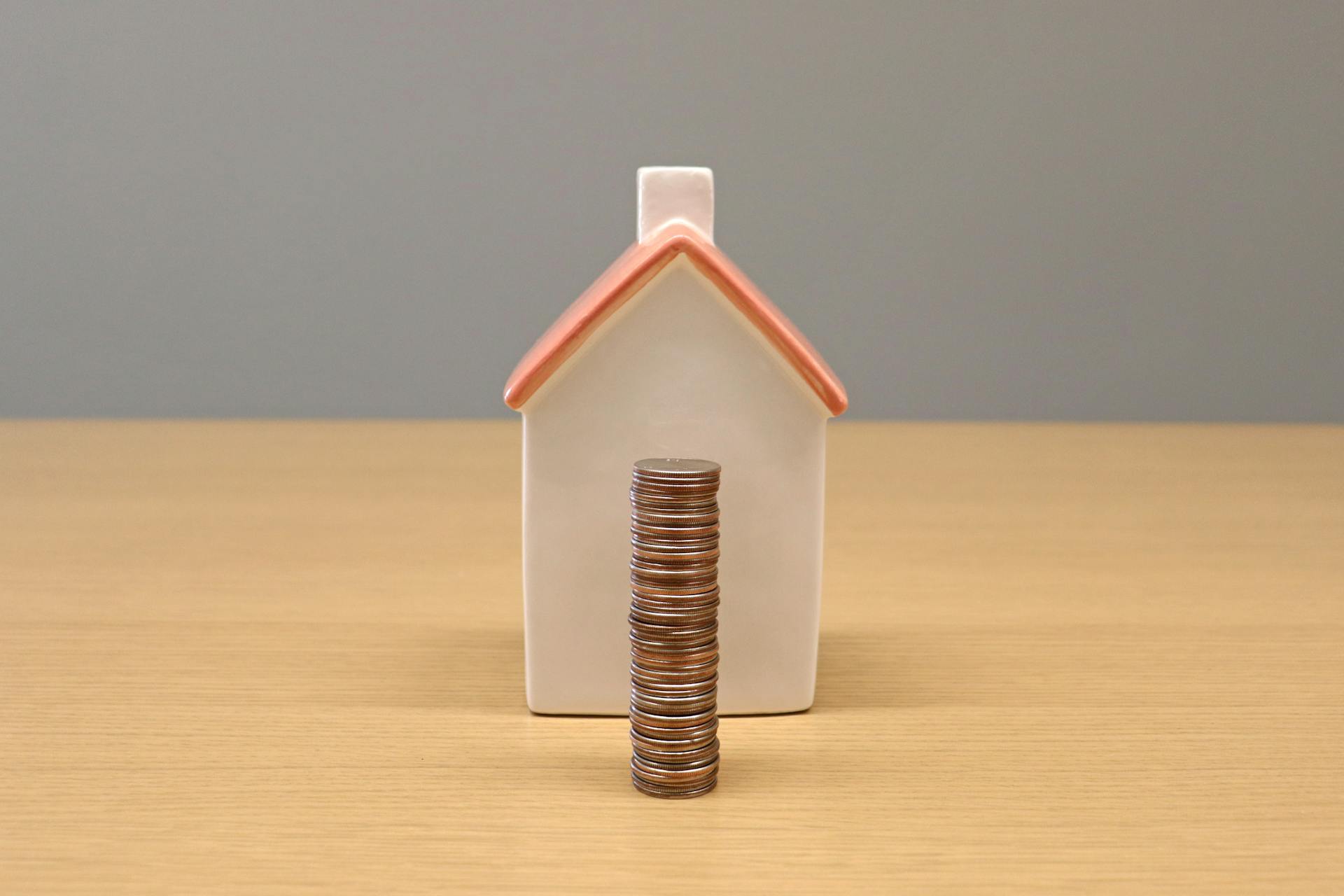 A conceptual still life image of stacked coins in front of a porcelain house, symbolizing savings and investment.