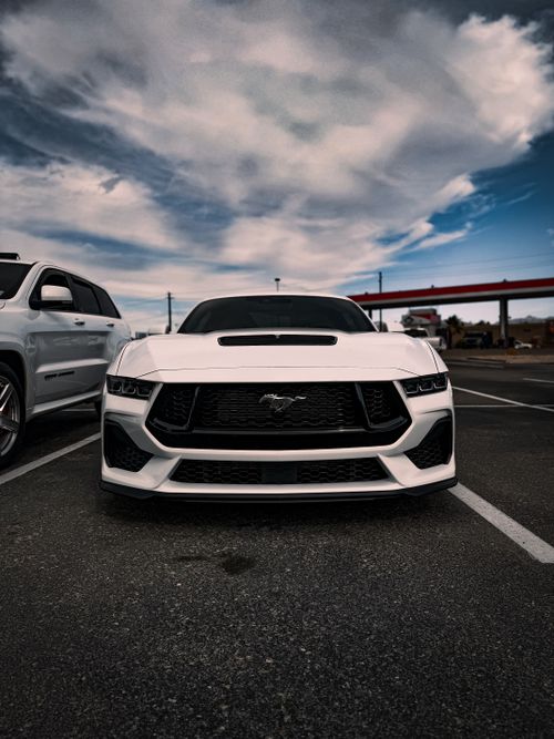 Free Front view of a stylish white sports car parked in an urban lot under a cloudy sky. Stock Photo