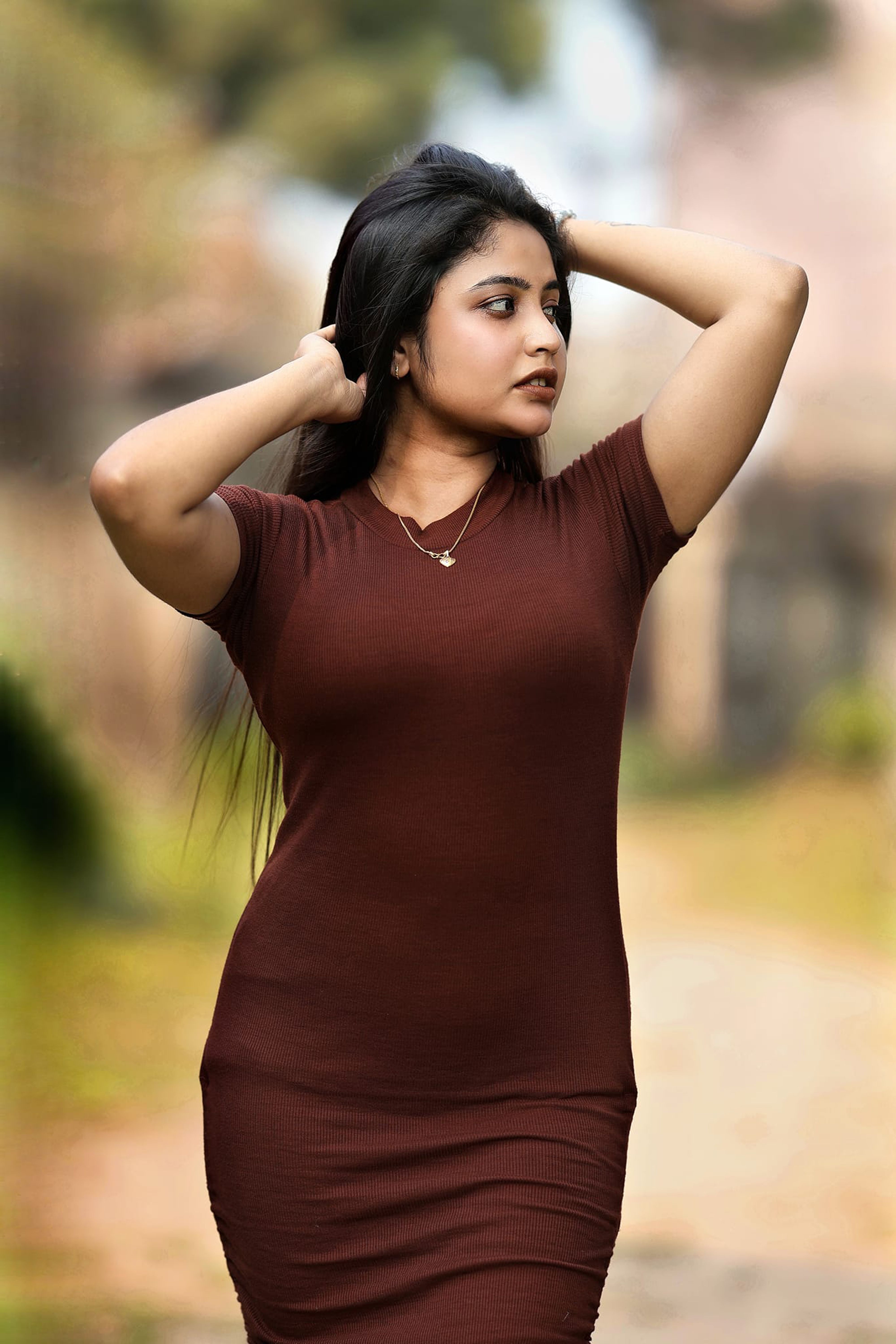 Fashionable young woman posing confidently in a brown dress outside.