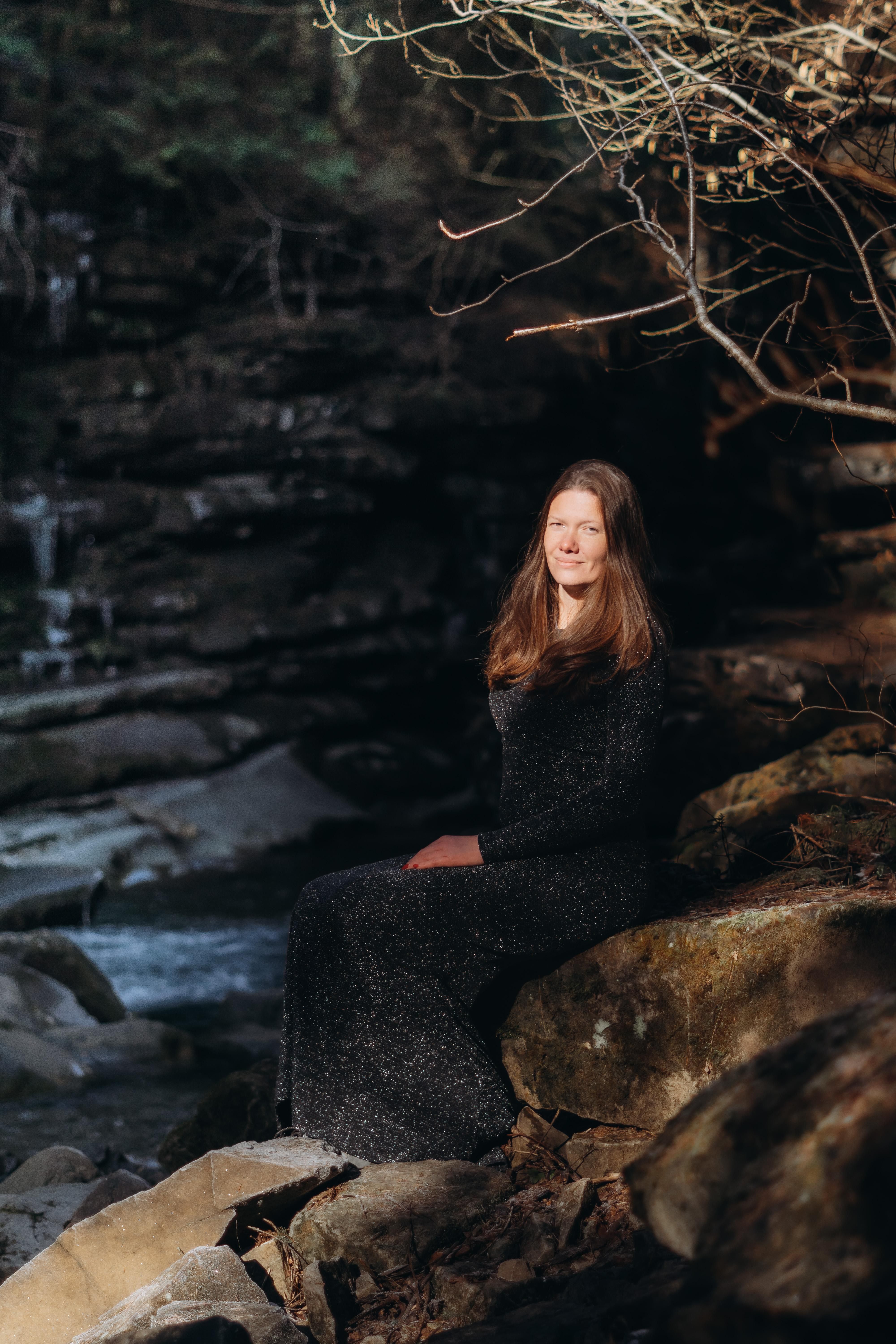 Woman in Black Dress Sitting on Rocks over Stream · Free Stock Photo