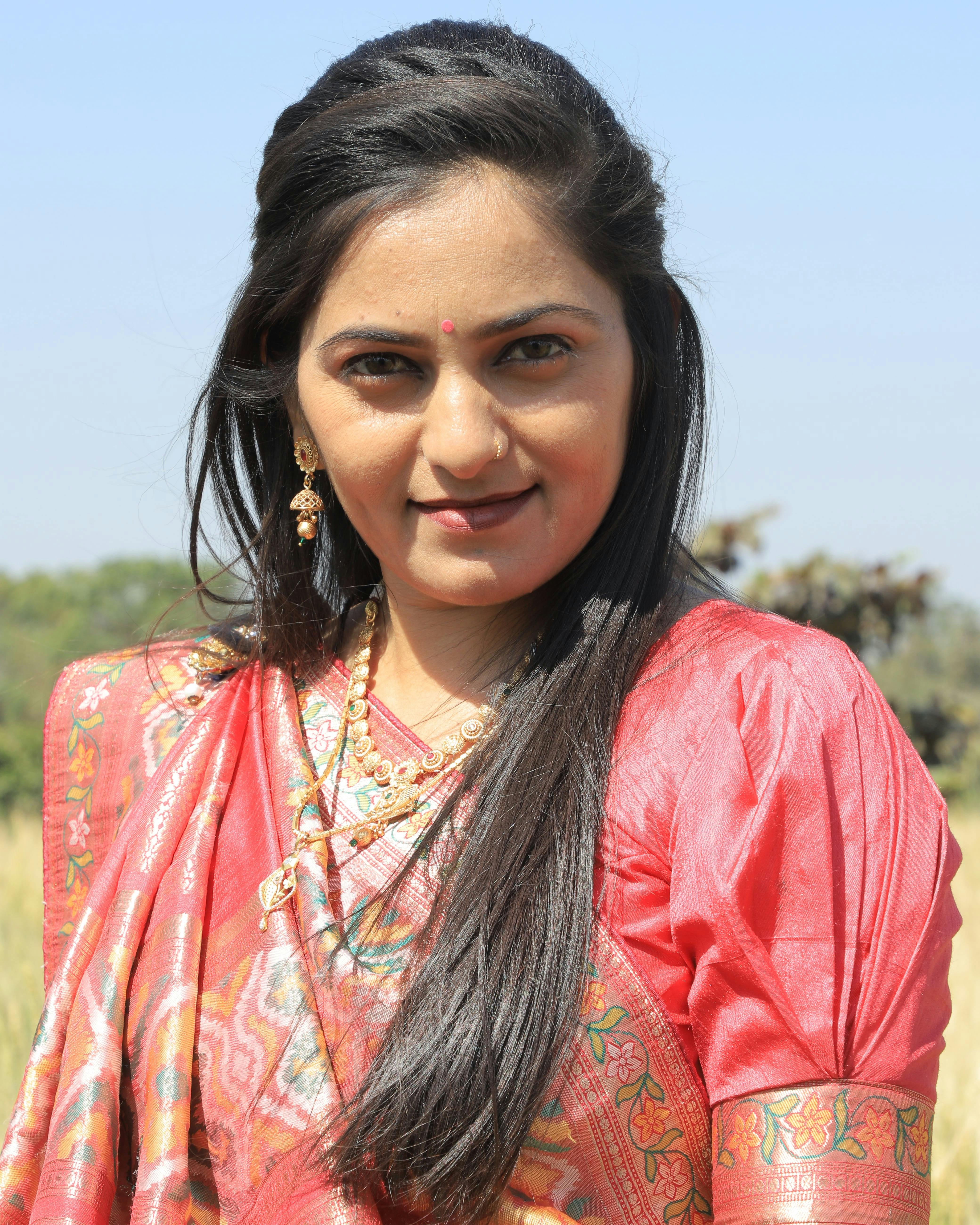 Portrait of a young South Asian woman wearing a red saree, captured outdoors in vibrant sunlight.