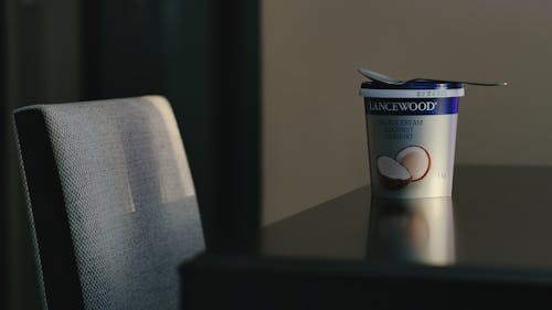 A yogurt cup sits on a table next to a chair