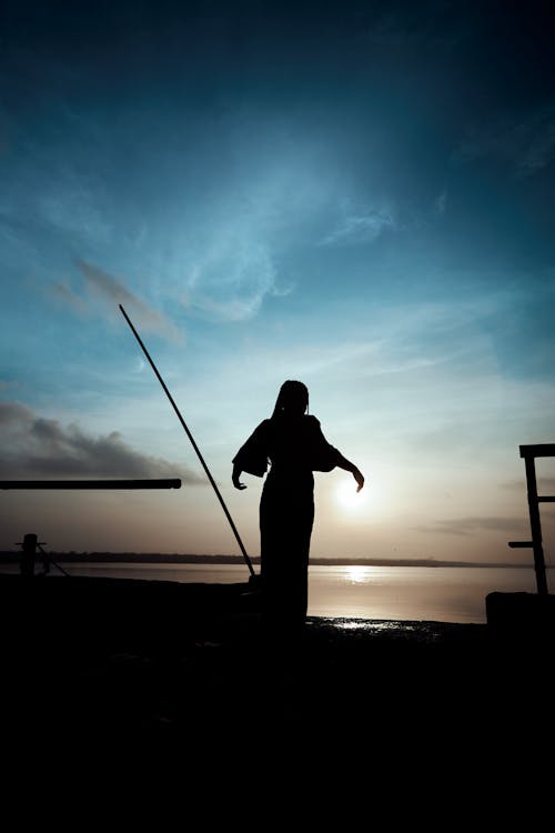 A silhouette of a woman standing on a dock with a fishing rod