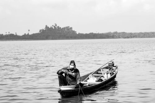 Free A lone fisherman in a wooden boat on a calm lake in a black and white composition. Stock Photo