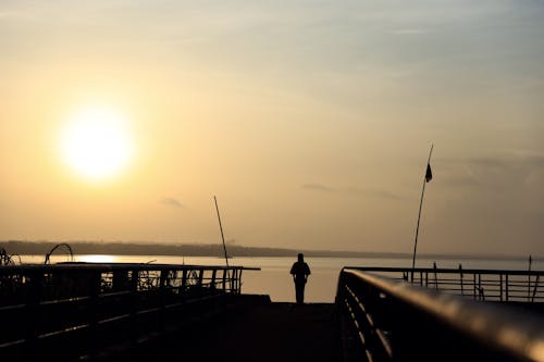 Silhouette of a Person Standing on a Pier at Sunset
