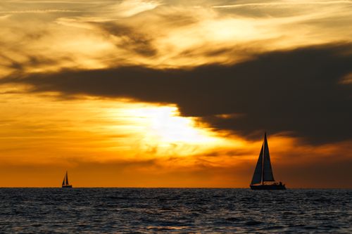 Free Beautiful sailboats cruising at sea under a dramatic orange sunset sky, perfect for travel and adventure themes. Stock Photo