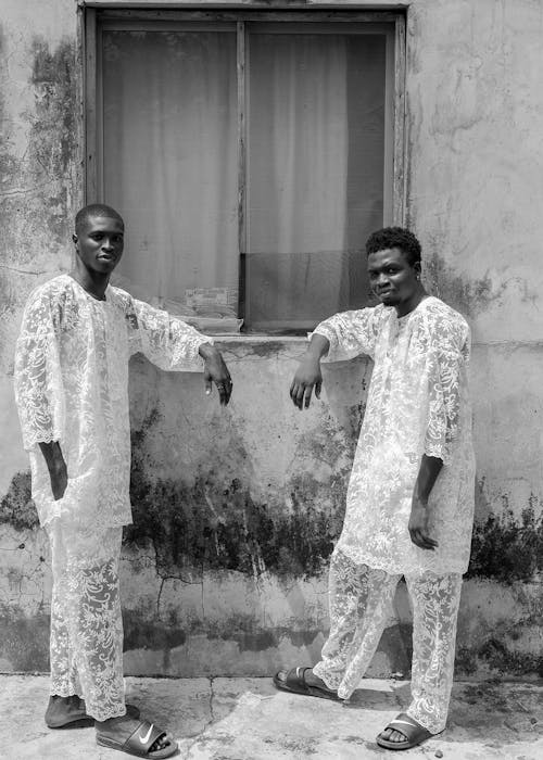 Two men in white clothes standing next to a window