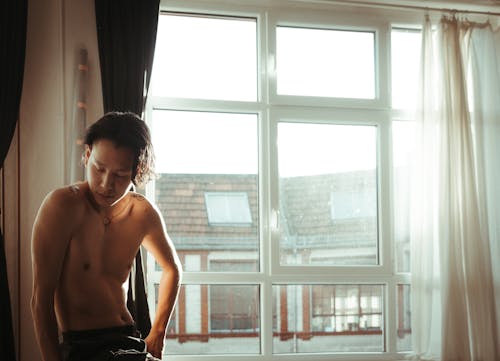 A shirtless man sitting on a window sill