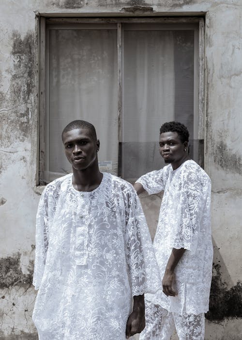 Two men in white clothes standing next to a window