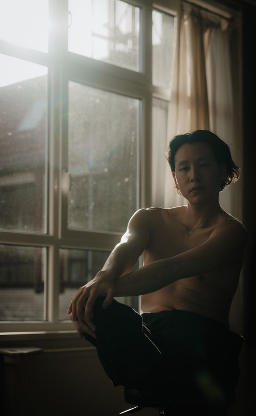 Free Artistic photo of a shirtless man sitting by a window with soft natural light. Stock Photo