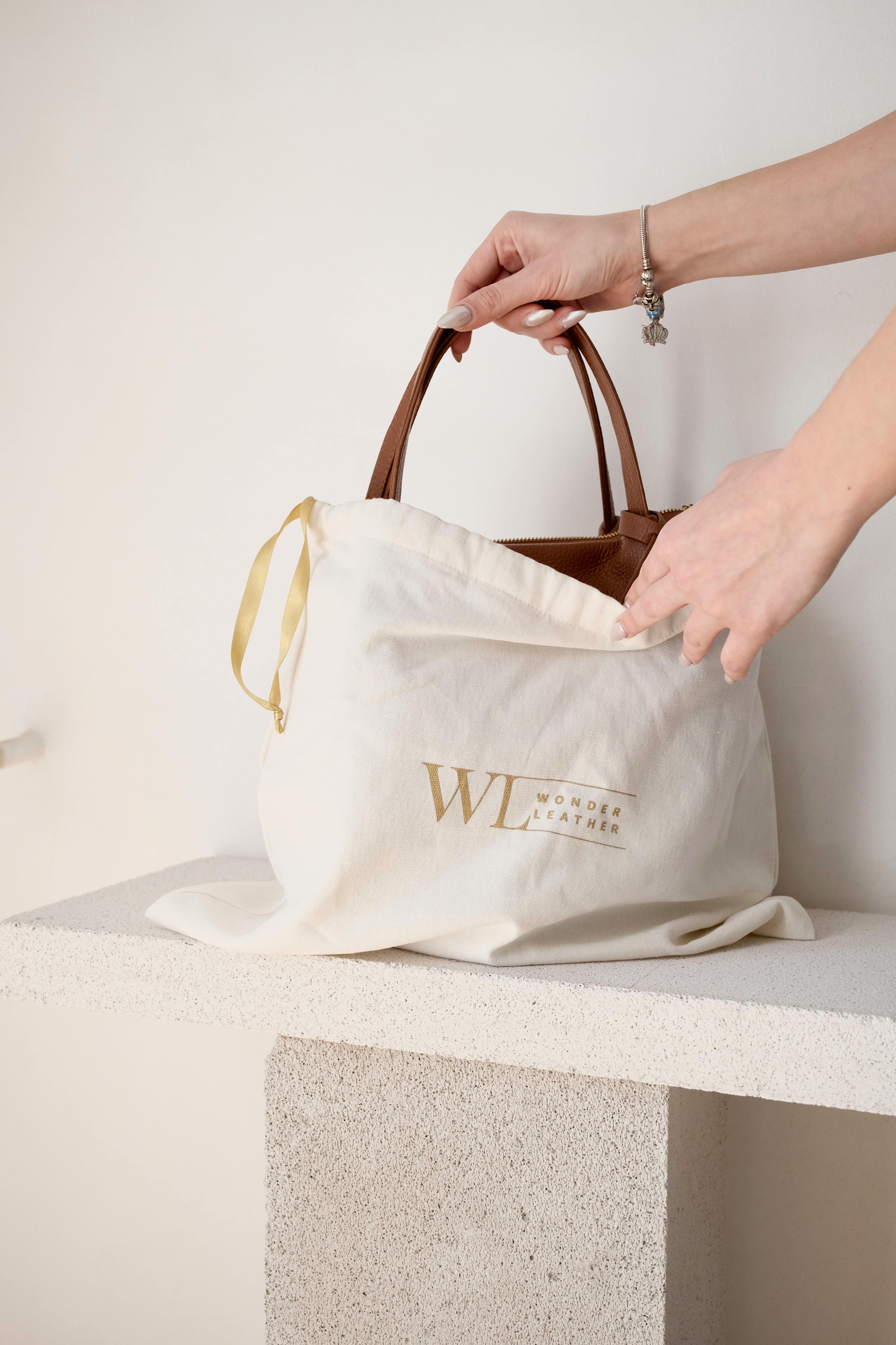 A woman's hands reveal a stylish handbag from a branded cloth cover atop a stone bench.