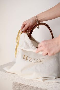 Hands unveiling a stylish brown leather handbag in a minimalistic setting.