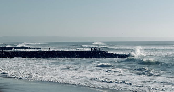 Silhouetted people on a breakwater against crashing ocean waves along Portugal's coast.