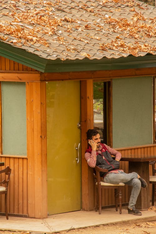 Seorang Pria Sedang Duduk Santai Sambil Berbicara Melalui Telepon Seluler Di Belakang Kafenya