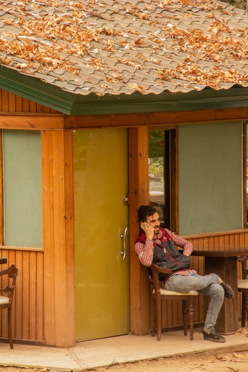 A man is sitting relaxed talking on a mobile phone at the back of his cafe