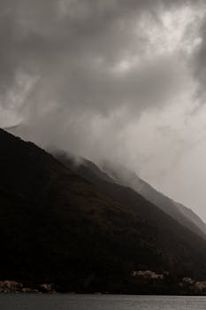 A moody, dramatic landscape of mountains in Kotor, Montenegro with clouds and fog.