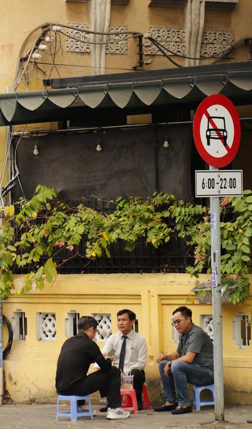 Three people sitting on a bench in front of a no parking sign
