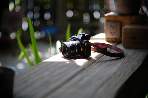 A camera sitting on a wooden table with a red strap