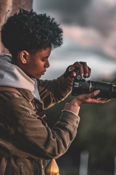 A young African woman with an afro hairstyle taking a photo outdoors using a DSLR camera.