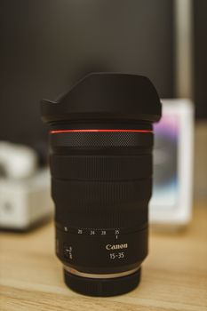 Close-up of a Canon lens standing on a wooden desk indoors, emphasizing detail and clarity.