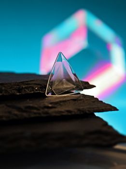 A glowing glass pyramid on textured rocks with abstract colors in the background.
