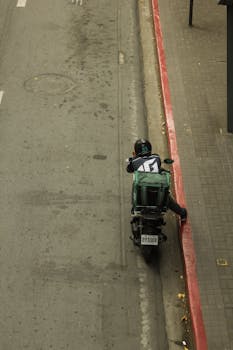 Aerial view of a food delivery scooter rider parked on a city street curb.