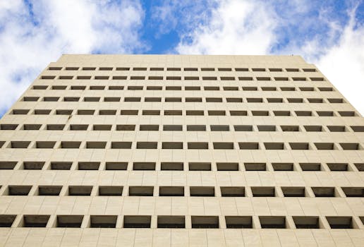 A geometric skyscraper facade with repeating windows rises against a bright blue sky.