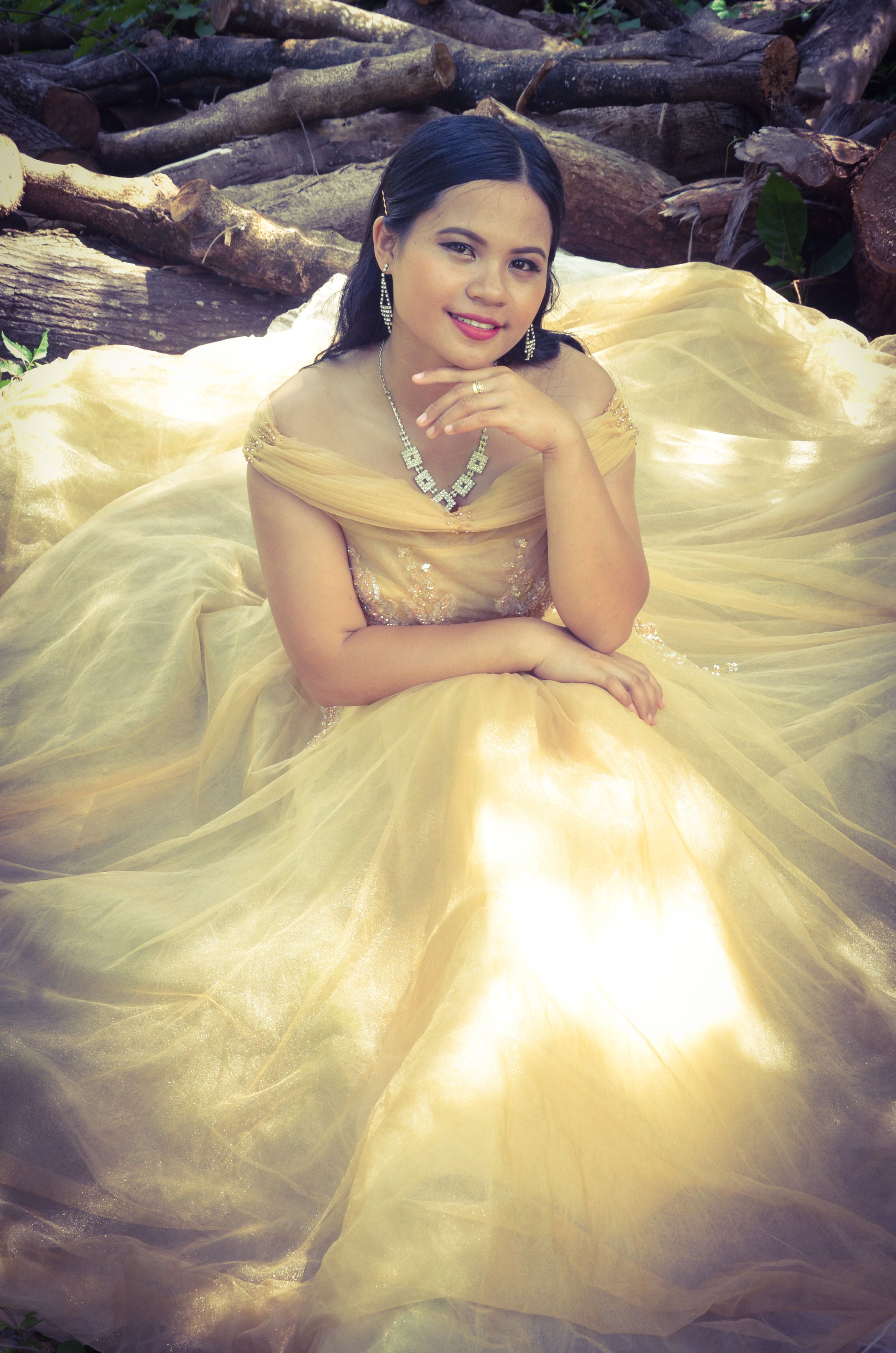 An elegant bride in a golden dress sitting outdoors, exuding sophistication.