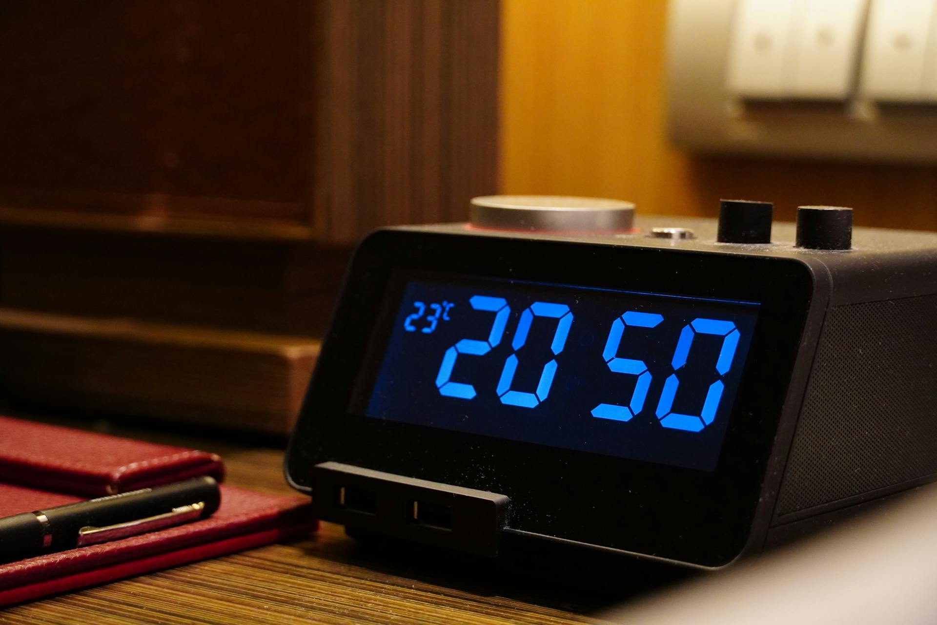 Close-up of a digital alarm clock displaying 20:50 and temperature on a wooden desk with a notepad.