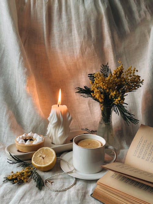 Burning Candle, Flowers, Cup with Lemons and Book