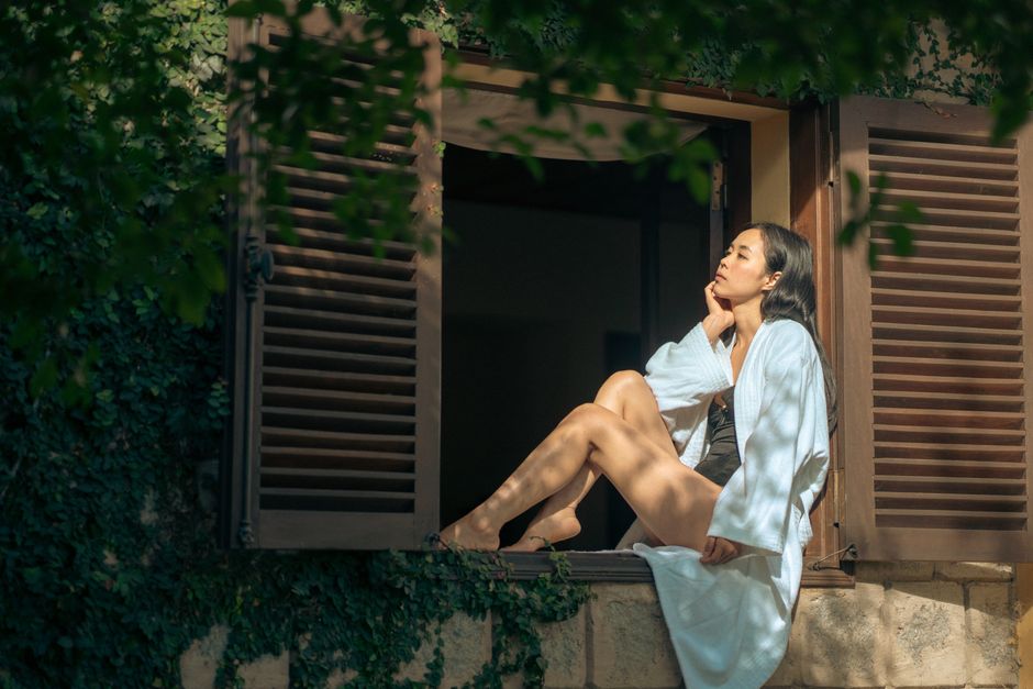 A woman in a bathrobe peacefully enjoys the sun by an open window in Dalat, Vietnam.