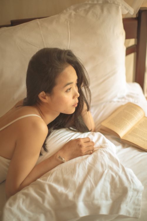 Free A serene moment with a woman reading in bed, surrounded by soft light. Stock Photo