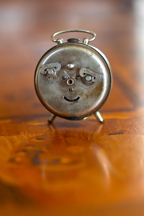 A small silver alarm clock with a face on it