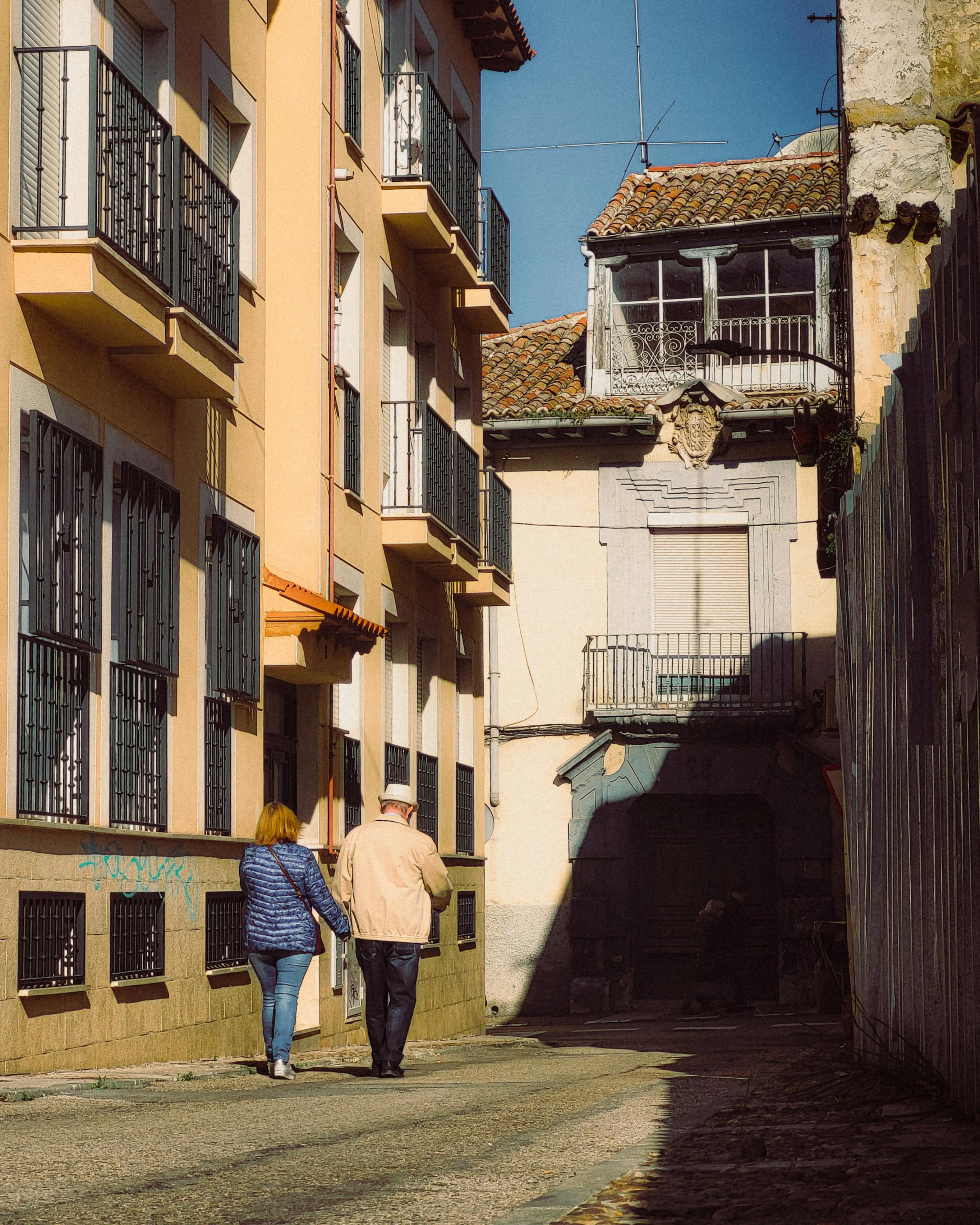 A couple walking hand-in-hand through a charming sunlit alley in Madrid, Spain.