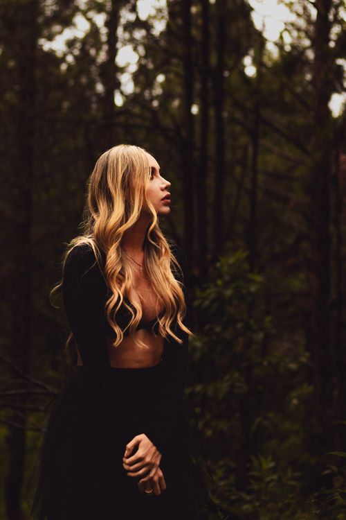 Free A woman stands gracefully in a forest, showcasing elegant fashion and serene beauty. Stock Photo