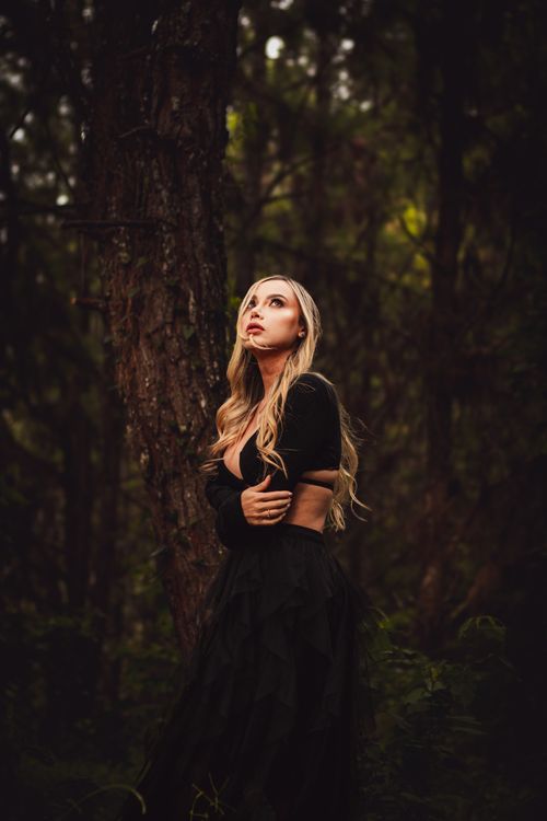 Free A blonde woman in elegant black attire gazing upwards in a dense Colombian forest setting. Stock Photo