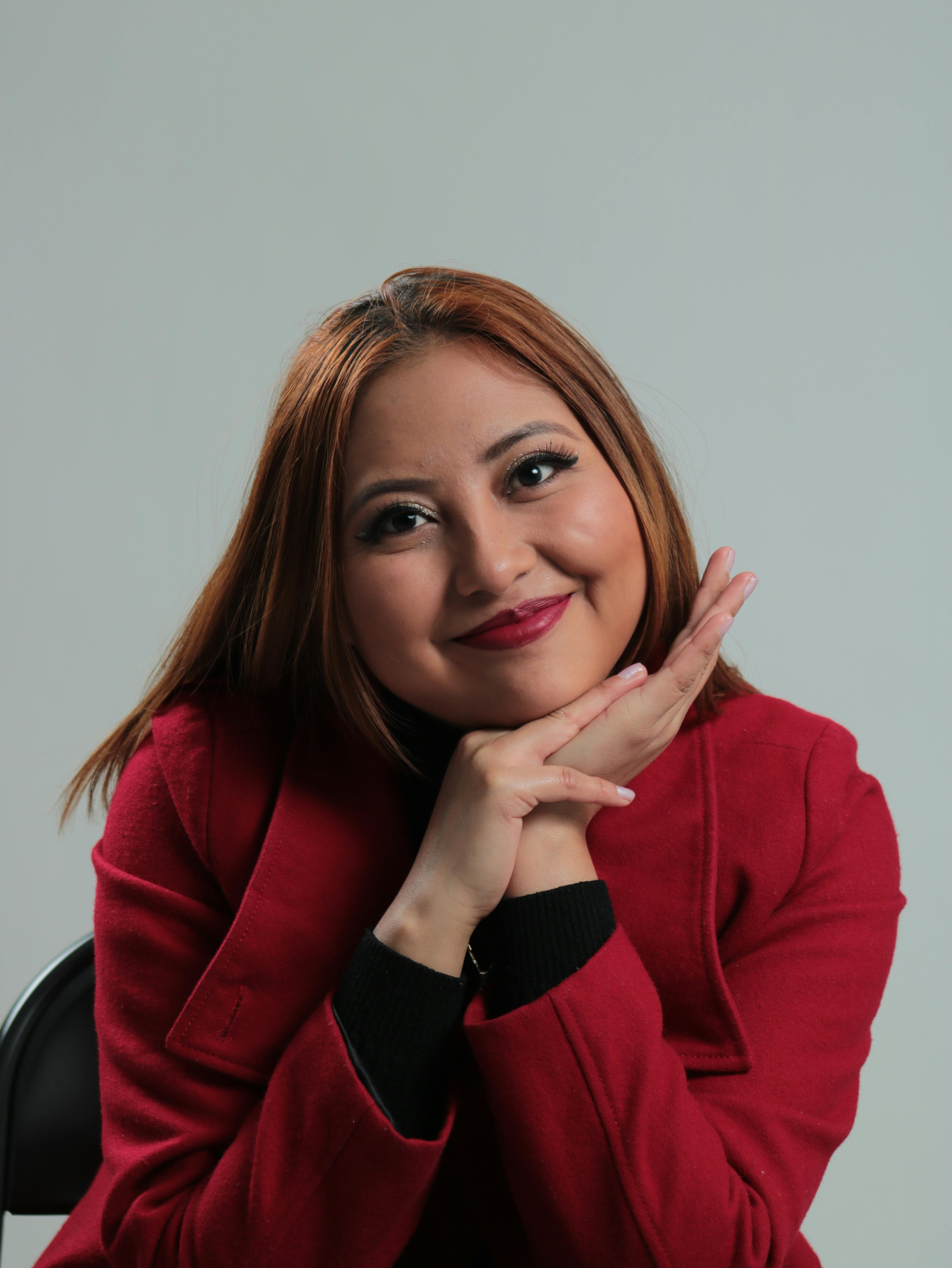 Discover the charm in this portrait of a woman smiling in a red jacket against a gray studio background.
