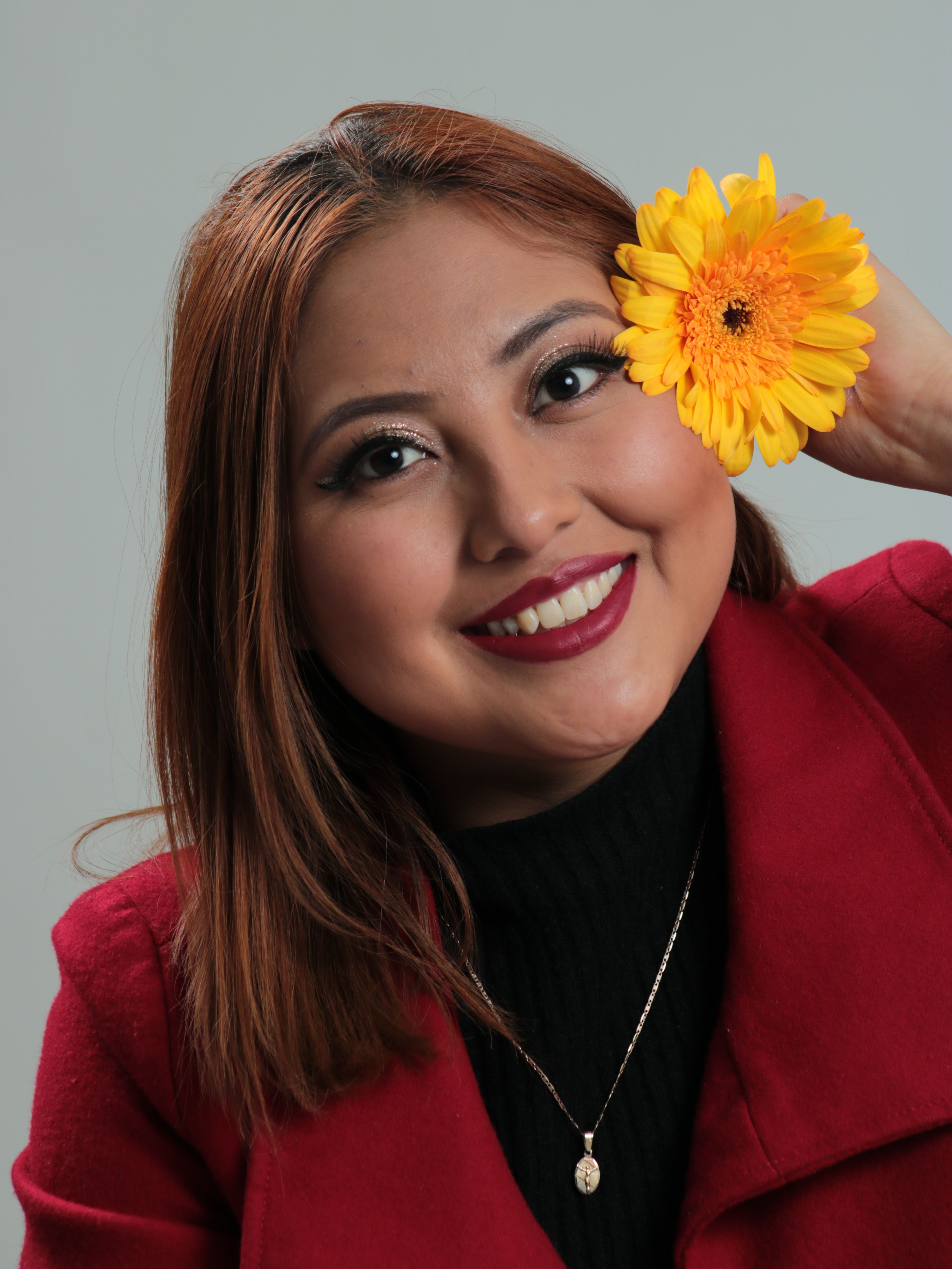 Portrait of a cheerful woman holding a yellow flower, wearing a red coat and necklace.
