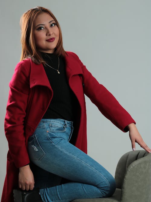 A woman in jeans and a red coat sitting on a chair