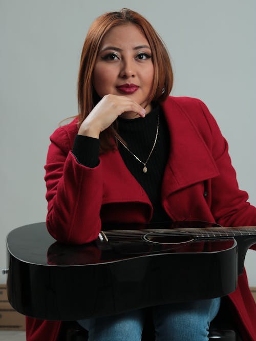 A woman in red jacket holding a guitar