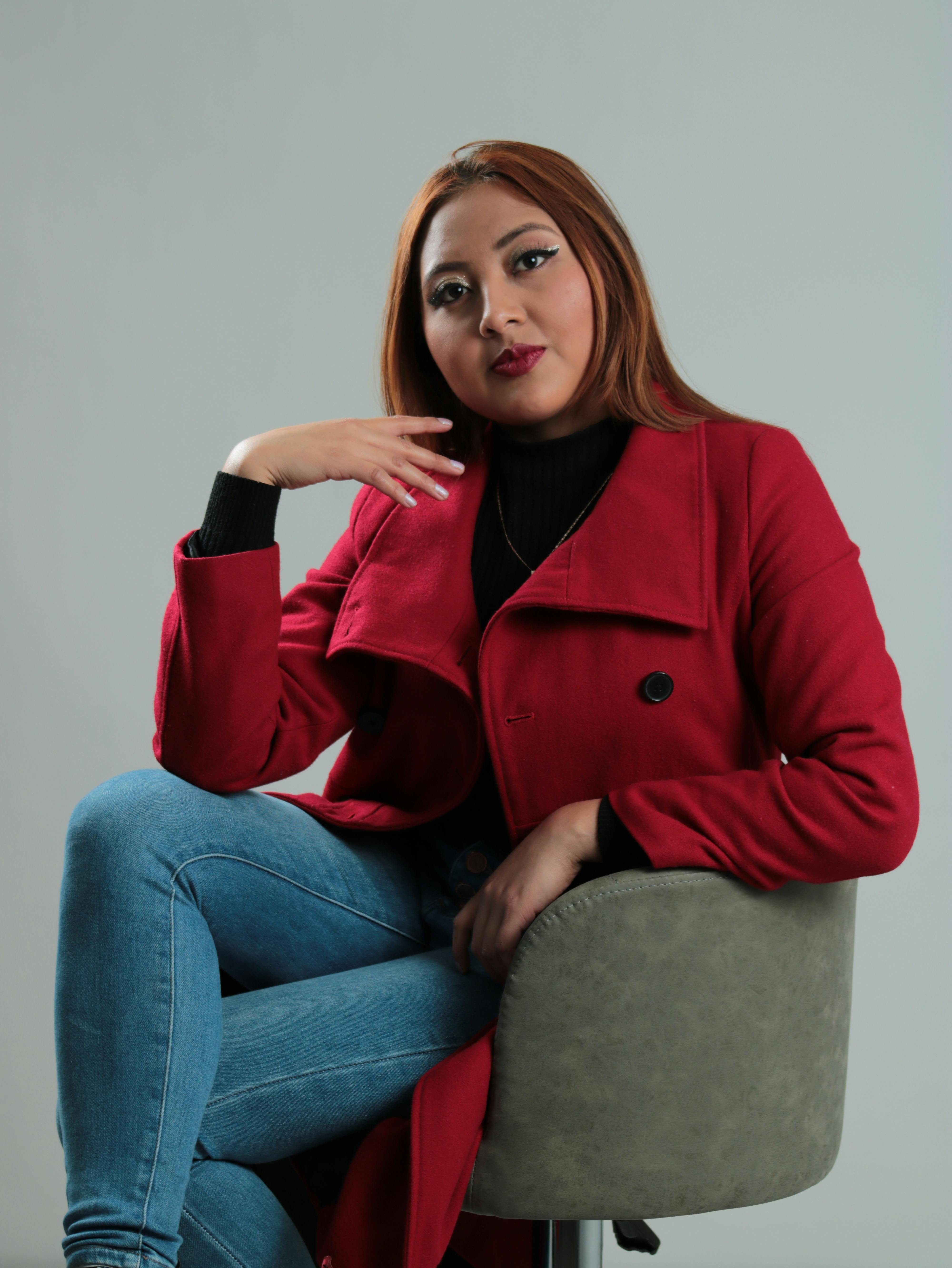 Portrait of a woman in a red coat sitting in a studio setting, showcasing fashion in a modern style.