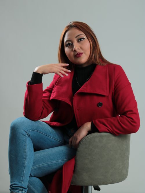 Free Portrait of a woman in a red coat sitting in a studio setting, showcasing fashion in a modern style. Stock Photo