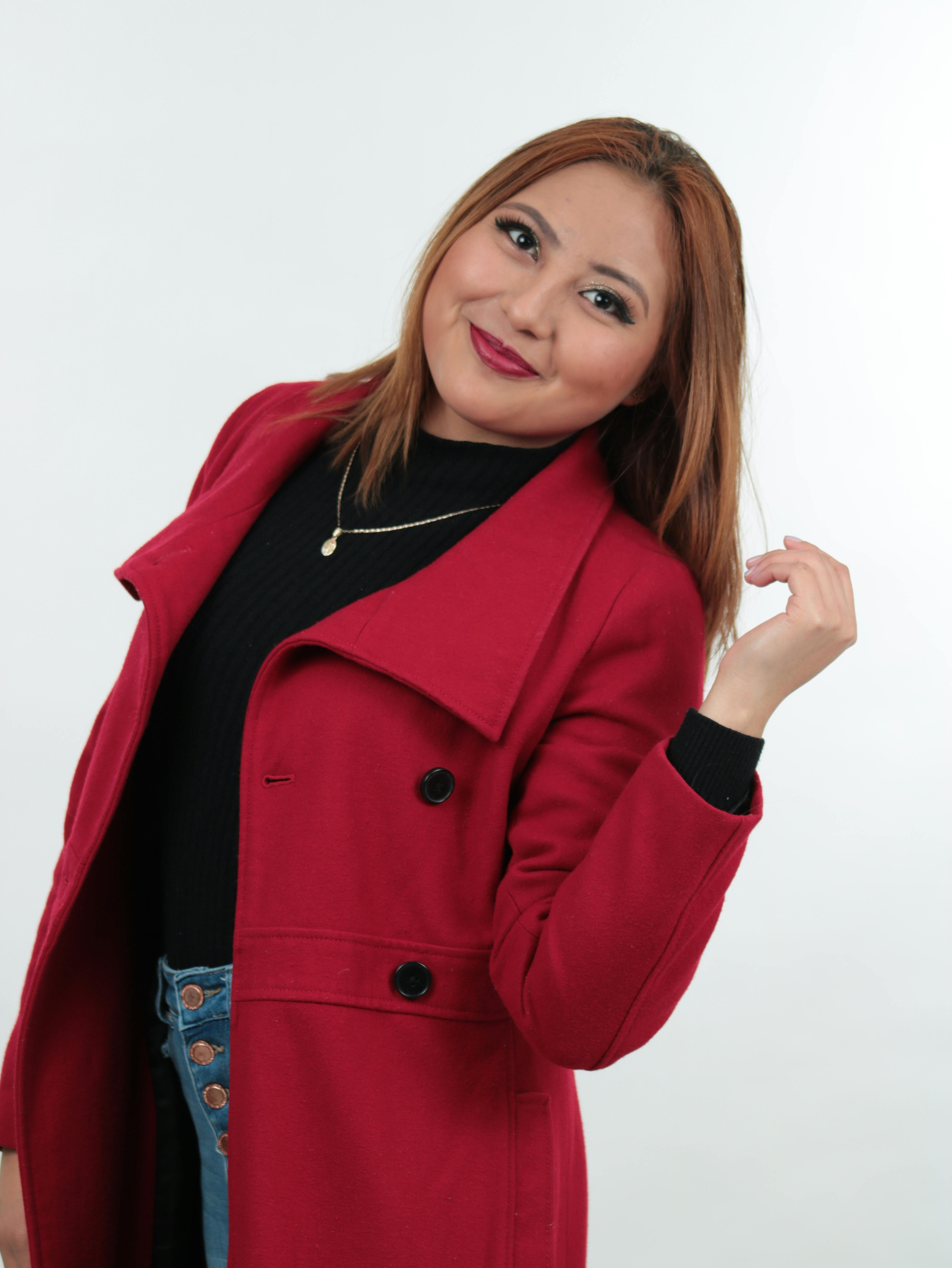 Portrait of a smiling woman in a fashionable red coat against a white background.