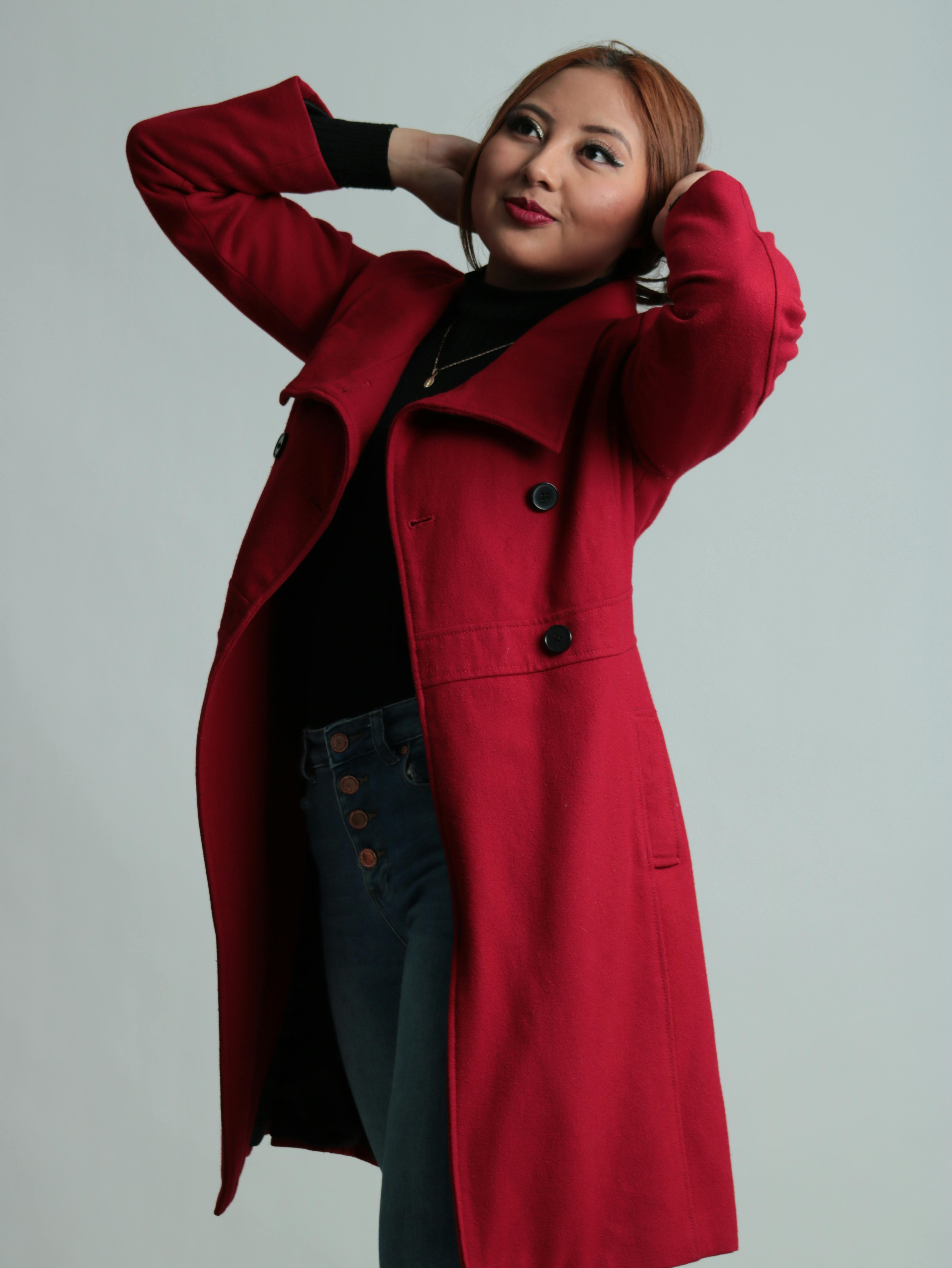 A stylish woman poses in a vibrant red coat against a white studio backdrop.